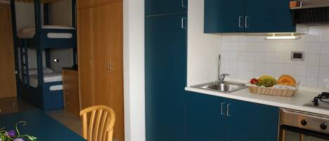 A compact kitchen with a sink, a dining area with a table and chair, and a bunk bed area.
