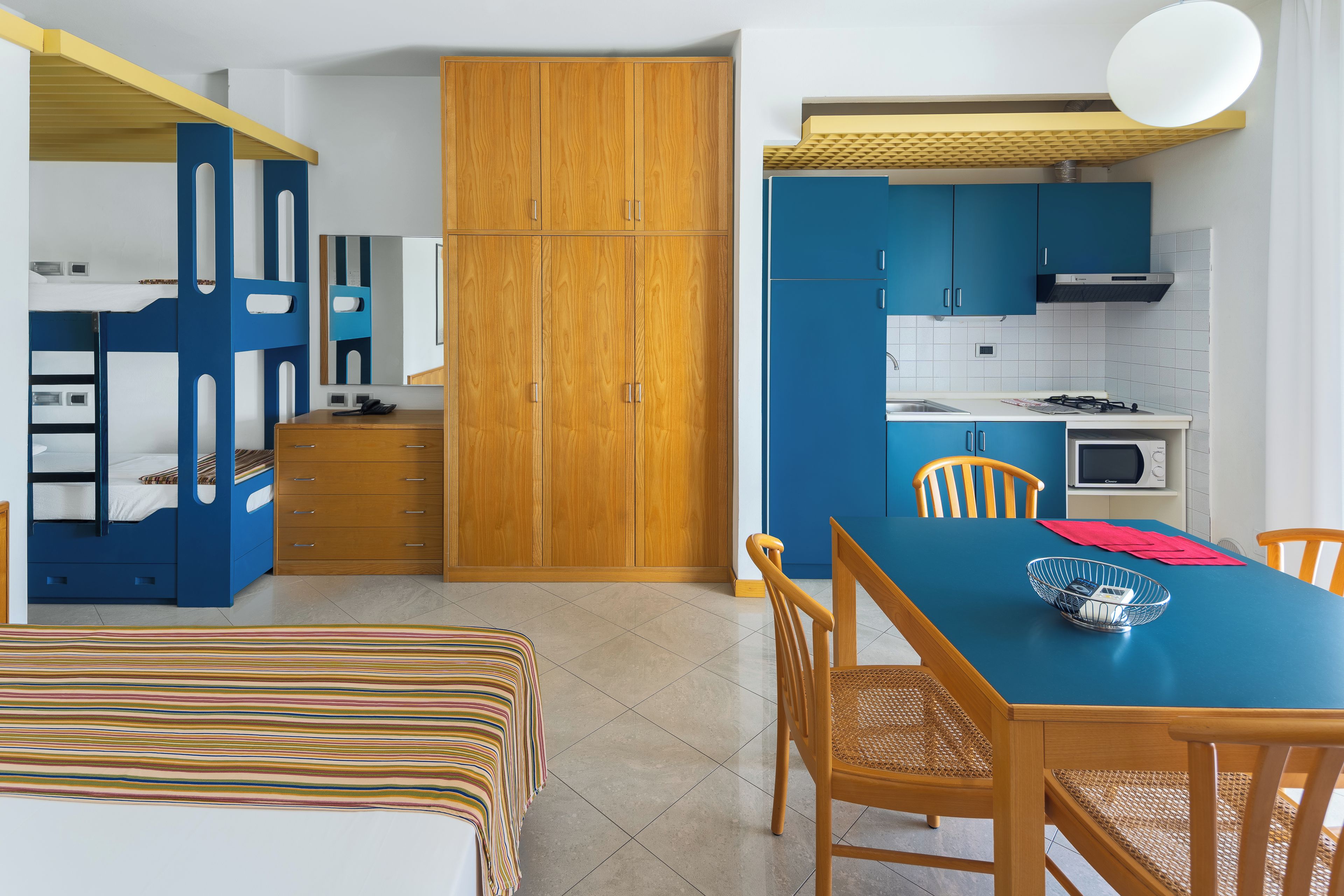 Habitación compacta con literas, un armario de madera, una mesa de comedor con sillas y una kitchenette.
