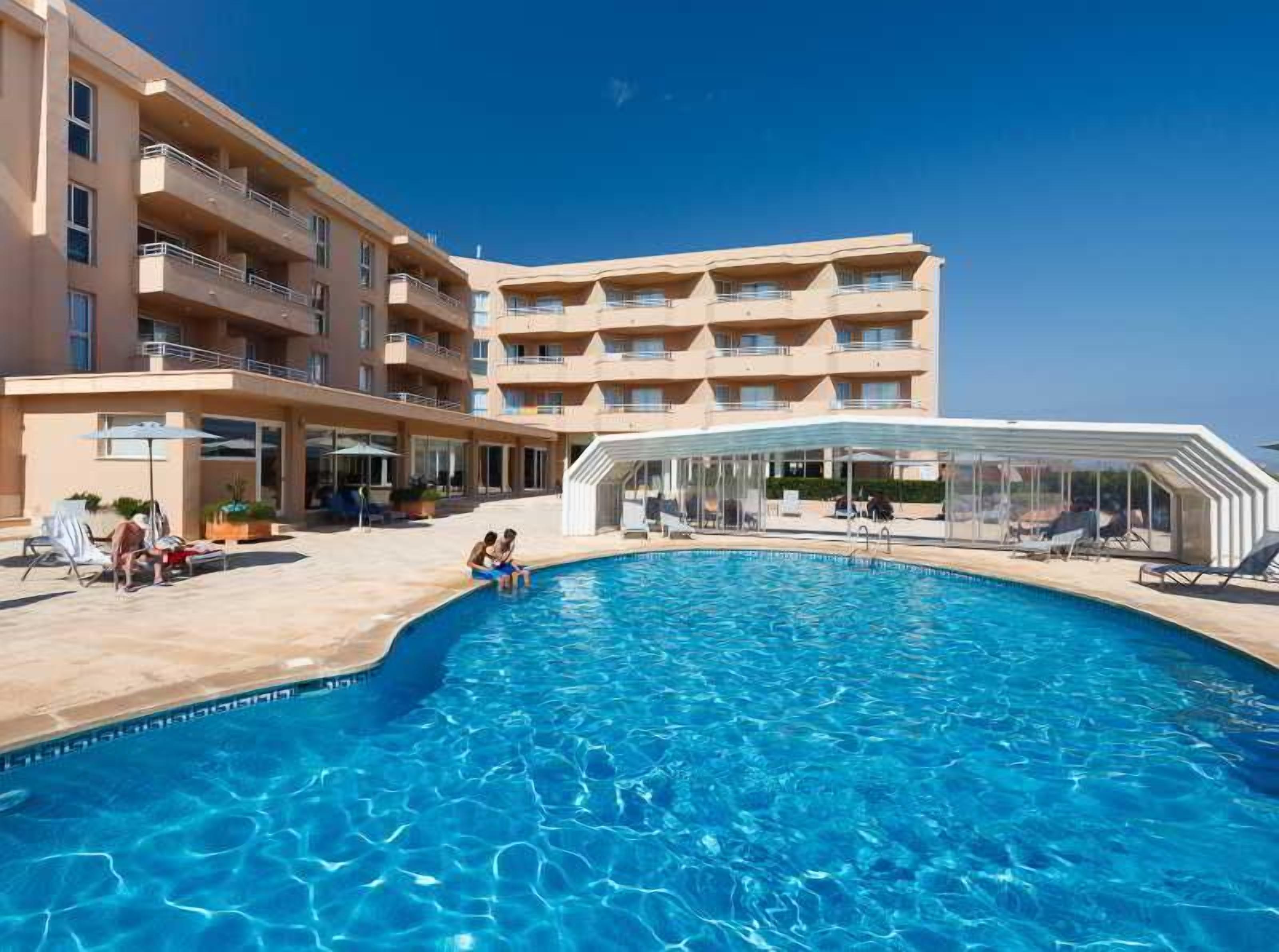 Un hotel amb piscina, zones d'estar a l'exterior i un edifici de diverses plantes.