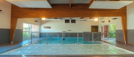 An indoor swimming pool with wooden beams, a diving board, and benches.