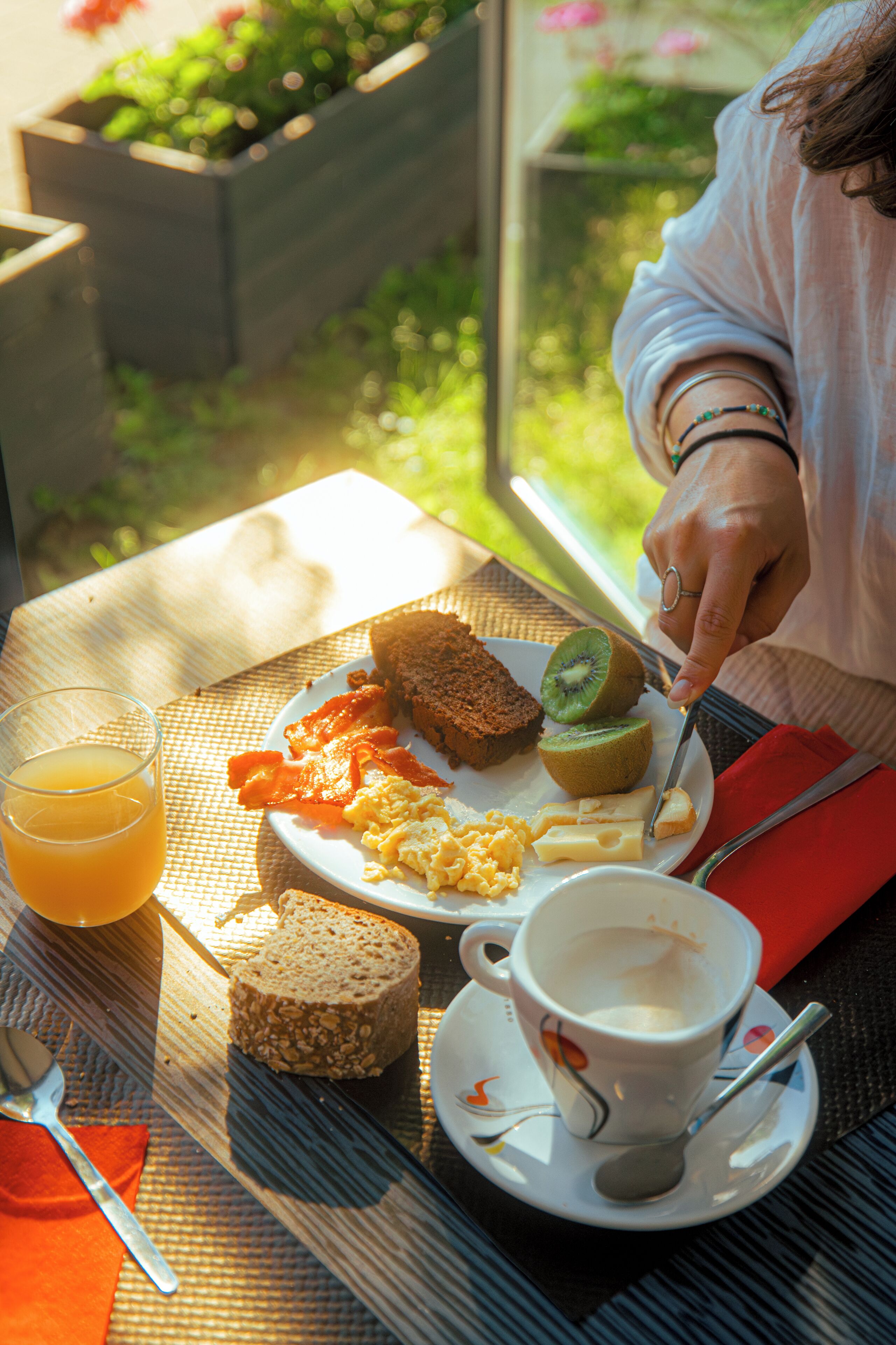 Un desayuno con tostadas, huevos, tocino, un kiwi y una taza de café sobre una mesa.