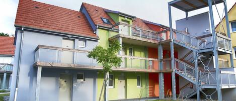 Un immeuble résidentiel à plusieurs étages, doté d’un toit recouvert de tuiles rouges, de balcons et d’un escalier.