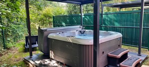 Un bain à remous installé à l’extérieur, avec une clôture verte et de la verdure en arrière-plan.