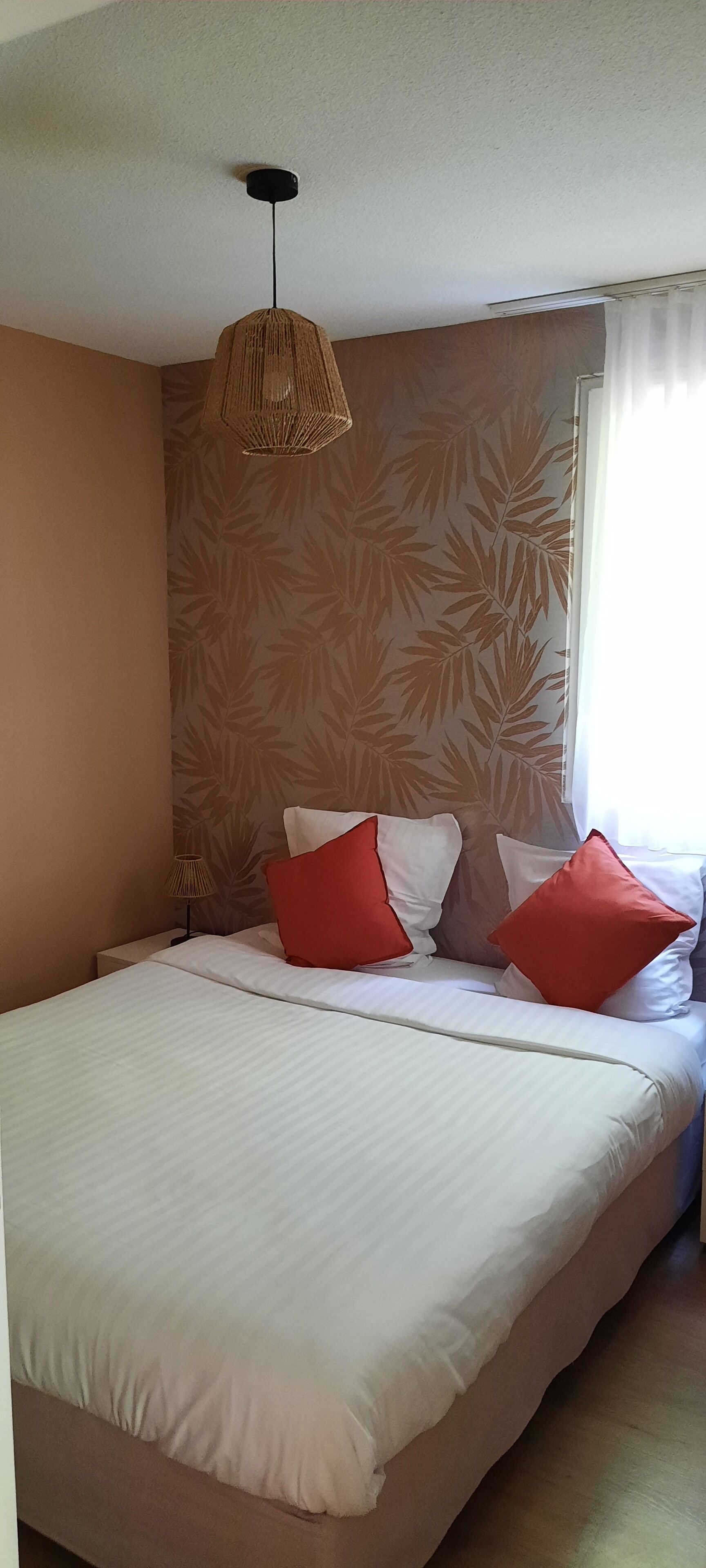 A bedroom with a bed, a hanging light fixture, a nightstand, and a window with curtains.