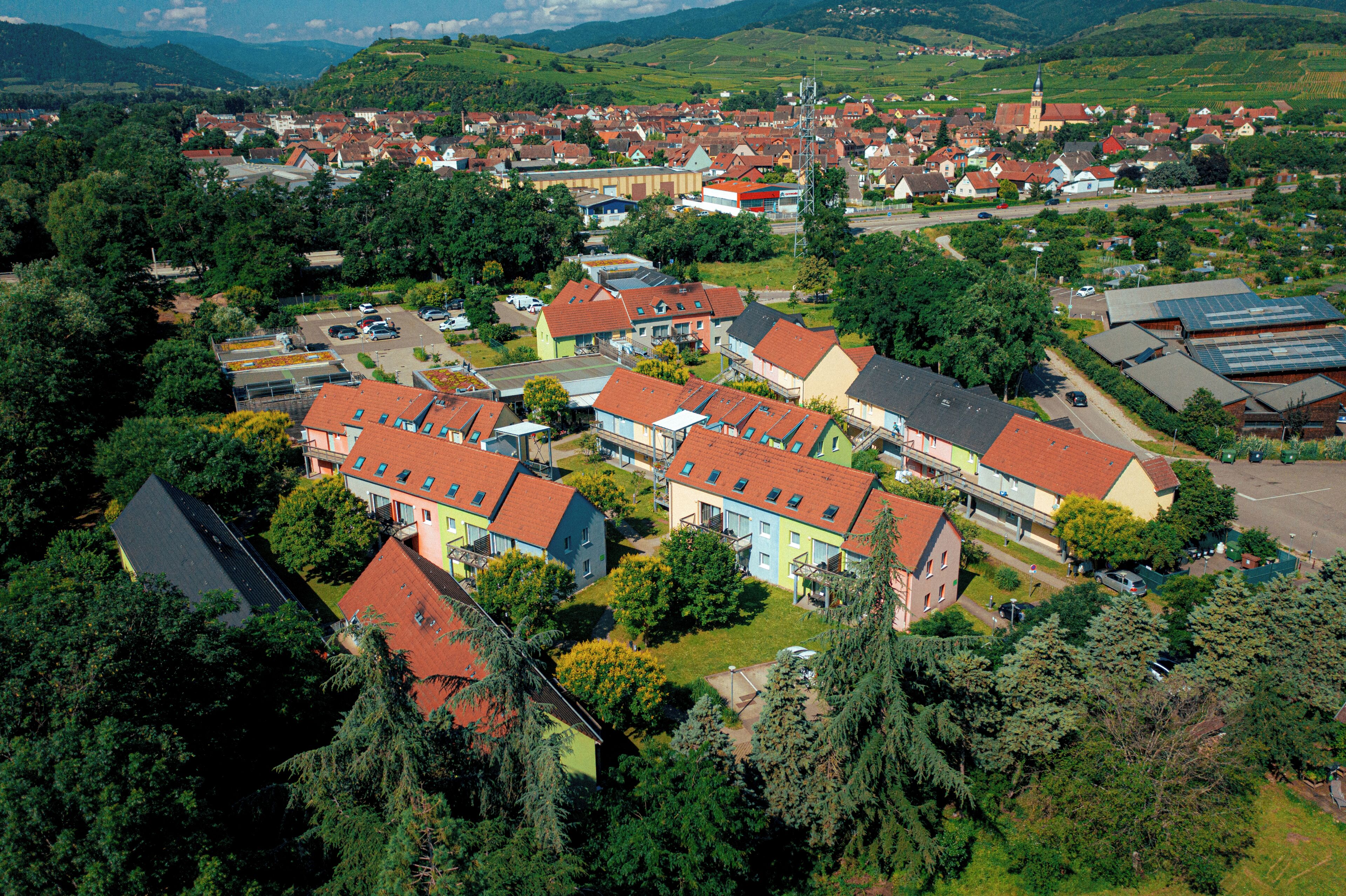 Vista aérea de una zona residencial con casas, algunas con paneles solares, rodeada de vegetación y colinas.
