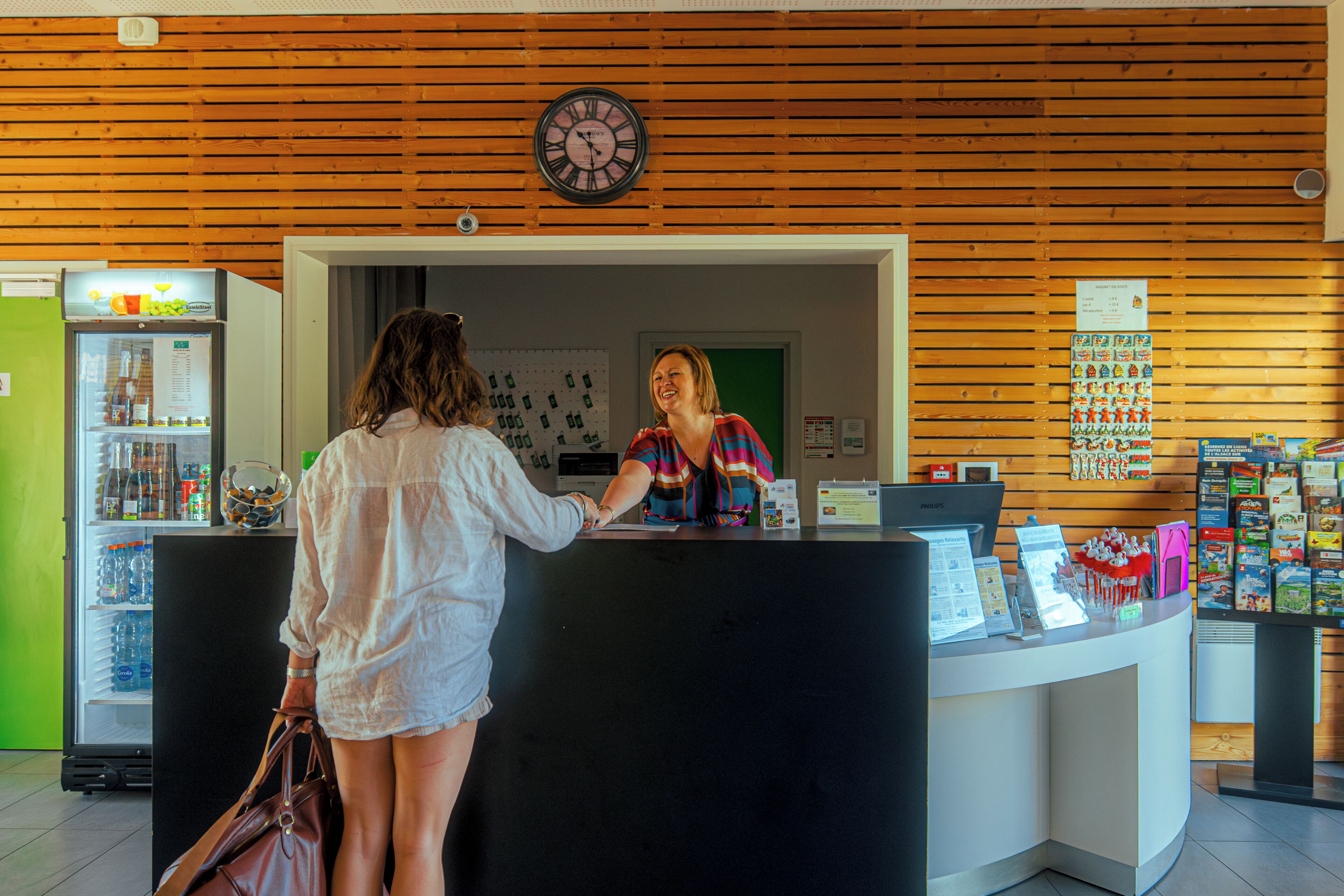 Zona de recepción con pared de madera, un reloj, un refrigerador y mostrador con diversos artículos.