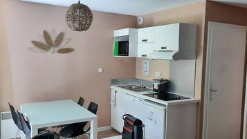 A compact kitchen with a white table and chairs, a microwave, a stove, and a refrigerator.