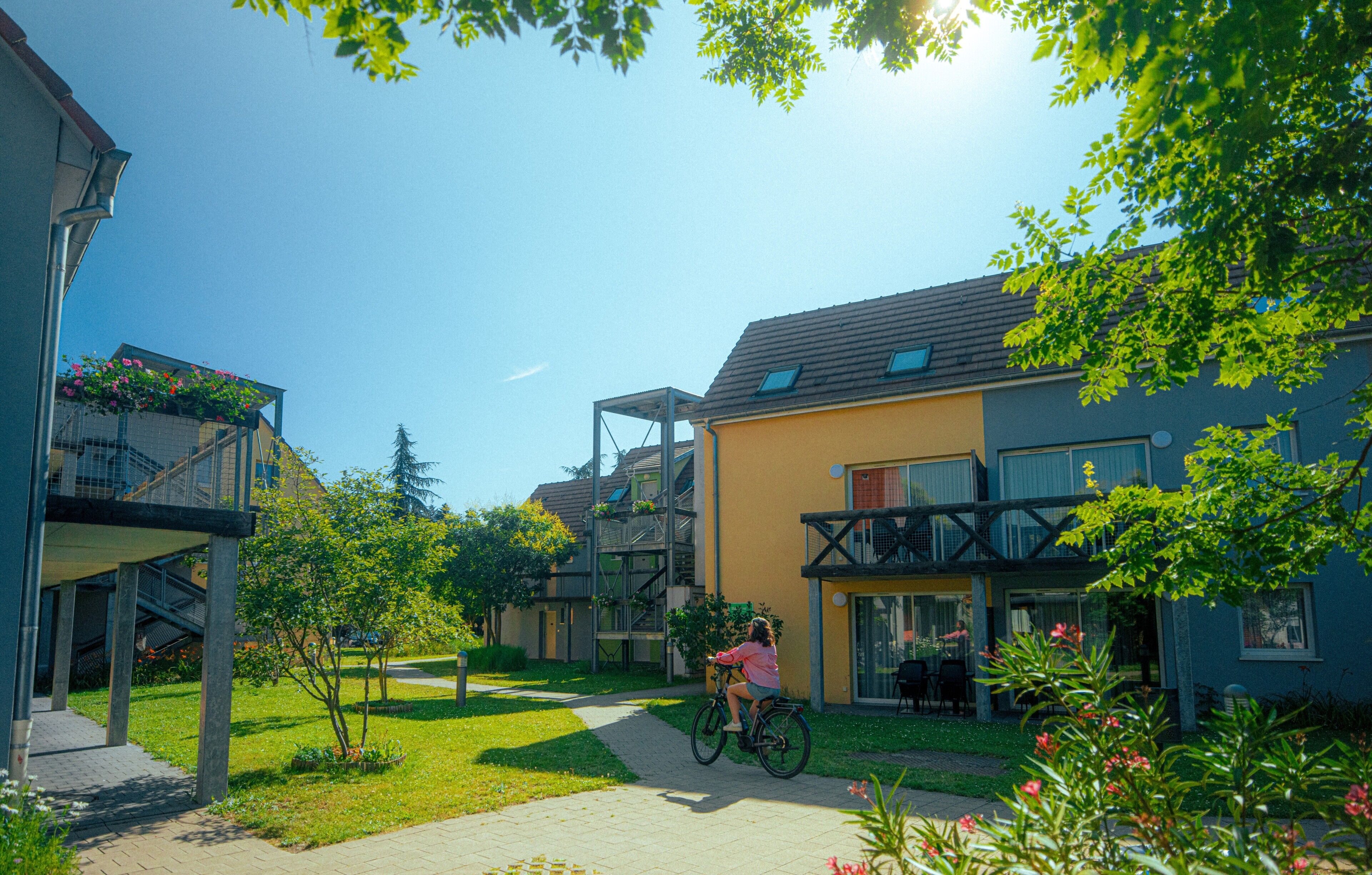 Un edificio residenziale con un balcone, un vialetto e una persona che va in bicicletta.