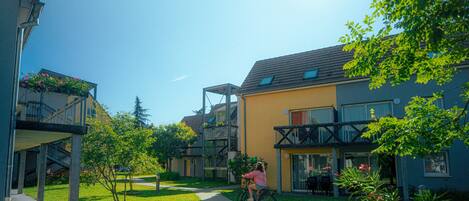A residential building with a balcony, a pathway, and a person riding a bicycle.
