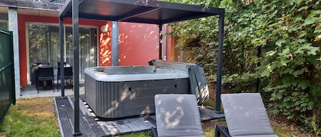 A hot tub under a pergola, surrounded by a patio with lounge chairs, a table, and chairs.