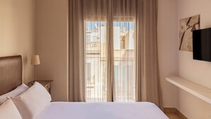 A hotel room with a bed, a nightstand with a lamp, a TV on the wall, and a window with curtains. - Gran de Gràcia Apartments (Barcelona)
