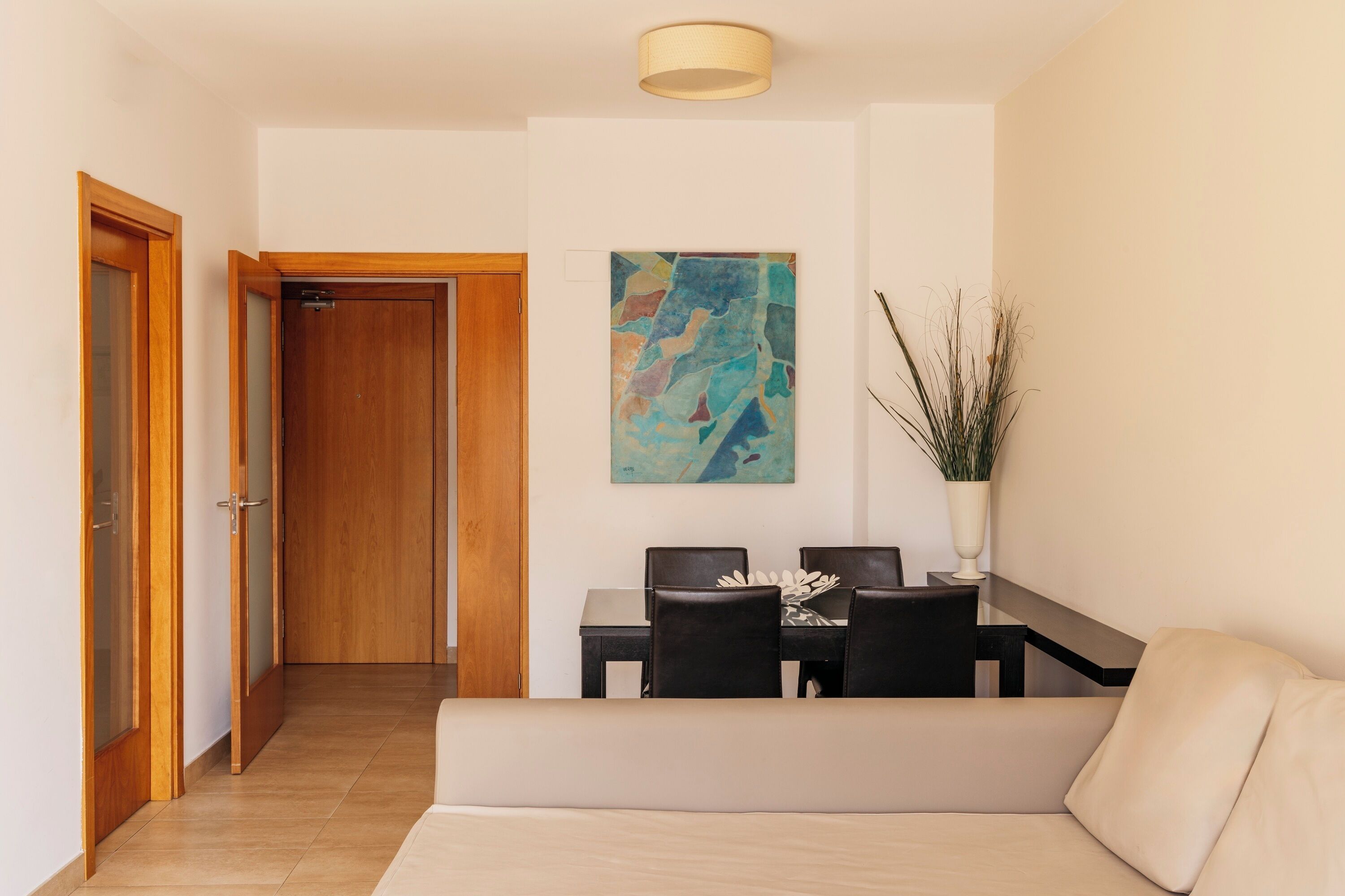 Een hotelkamer met een houten deur, een eettafel met stoelen, een bank, een schilderij aan de muur en een bloempot.