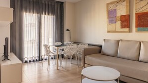A modern living room with a sofa, a dining table with chairs, a TV, and artwork on the wall. - Gran de Gràcia Apartments (Barcelona)