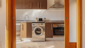 A compact kitchen with wooden cabinets, a built-in washing machine, a microwave, and an oven. - Gran de Gràcia Apartments (Barcelona)