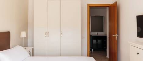 A bedroom with a bed, a wardrobe, a nightstand, a lamp, and a television.