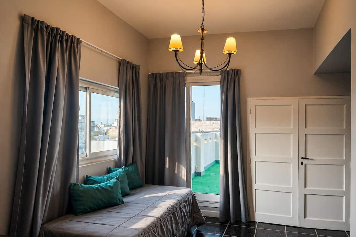 A bedroom with a bed, a chandelier, a window with curtains, and a door.