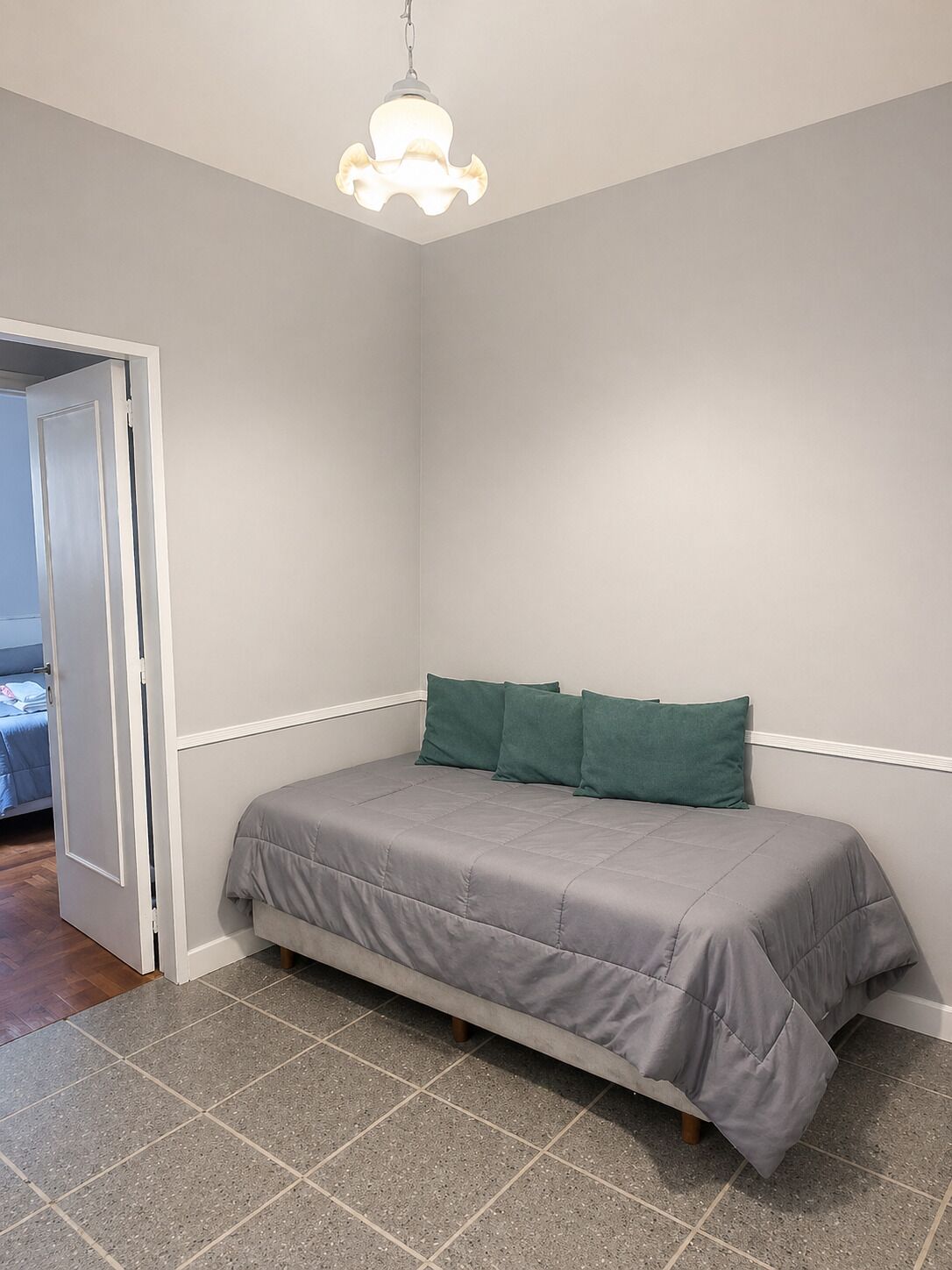 A bedroom with a bed, a door, and a hanging light fixture.
