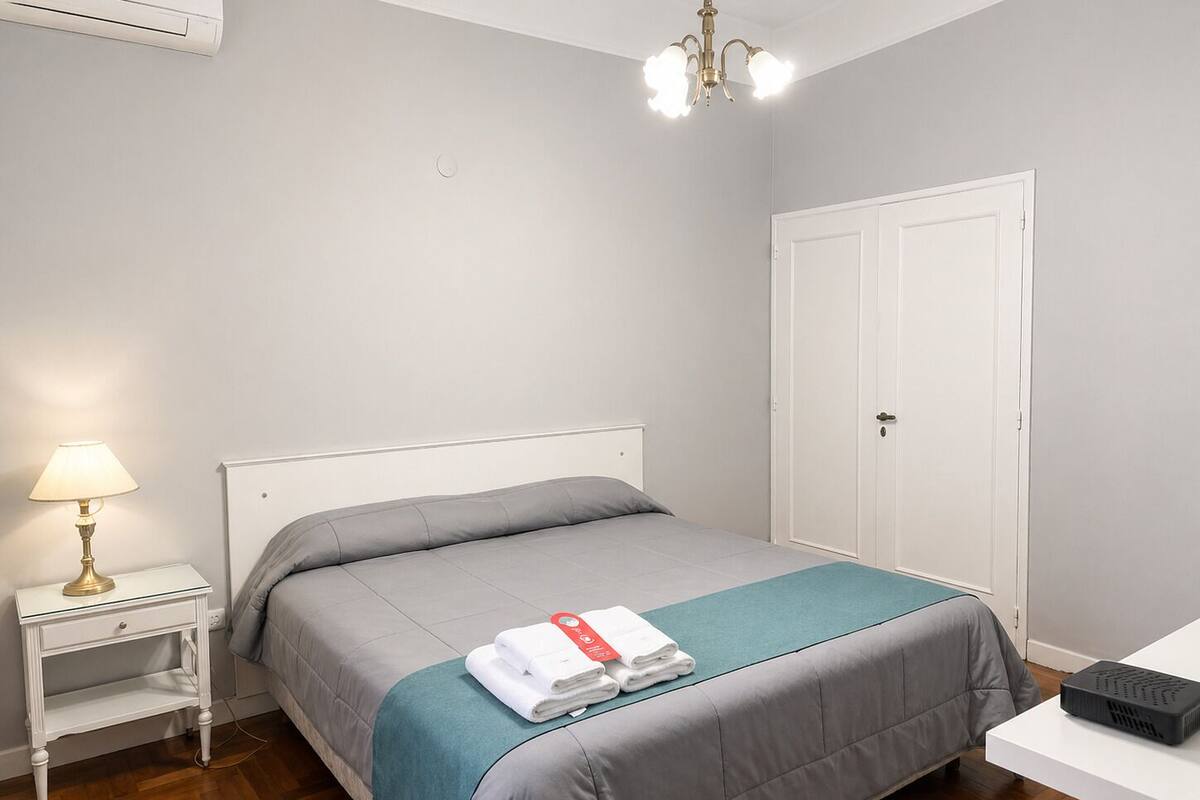 A bedroom with a bed, a nightstand, a lamp, a wardrobe, and a projector on a table.
