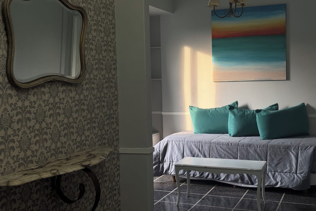 A bedroom with a bed, a bench, a mirror, a painting, and a chandelier.