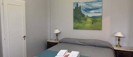 A hotel room with a bed, two bedside lamps, a painting on the wall, and a door.