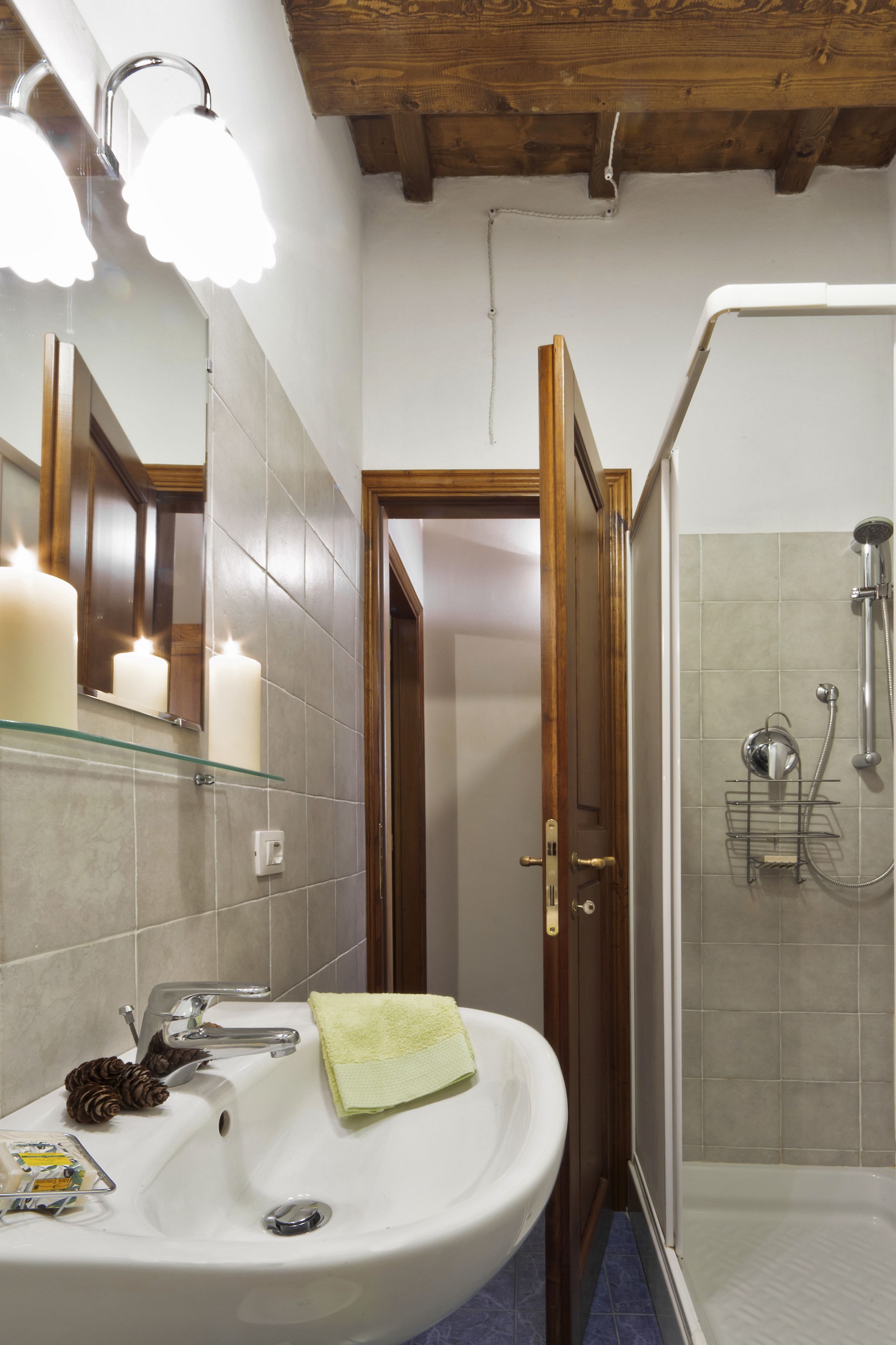 Een badkamer met een wit wastafelmeubel, een glazen plankje met kaarsen, een houten deur en een douchegedeelte.