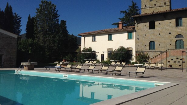 A pool area with lounge chairs and a stone building with a tower. - Castello di Pratelli (Figline e Incisa Valdarno)