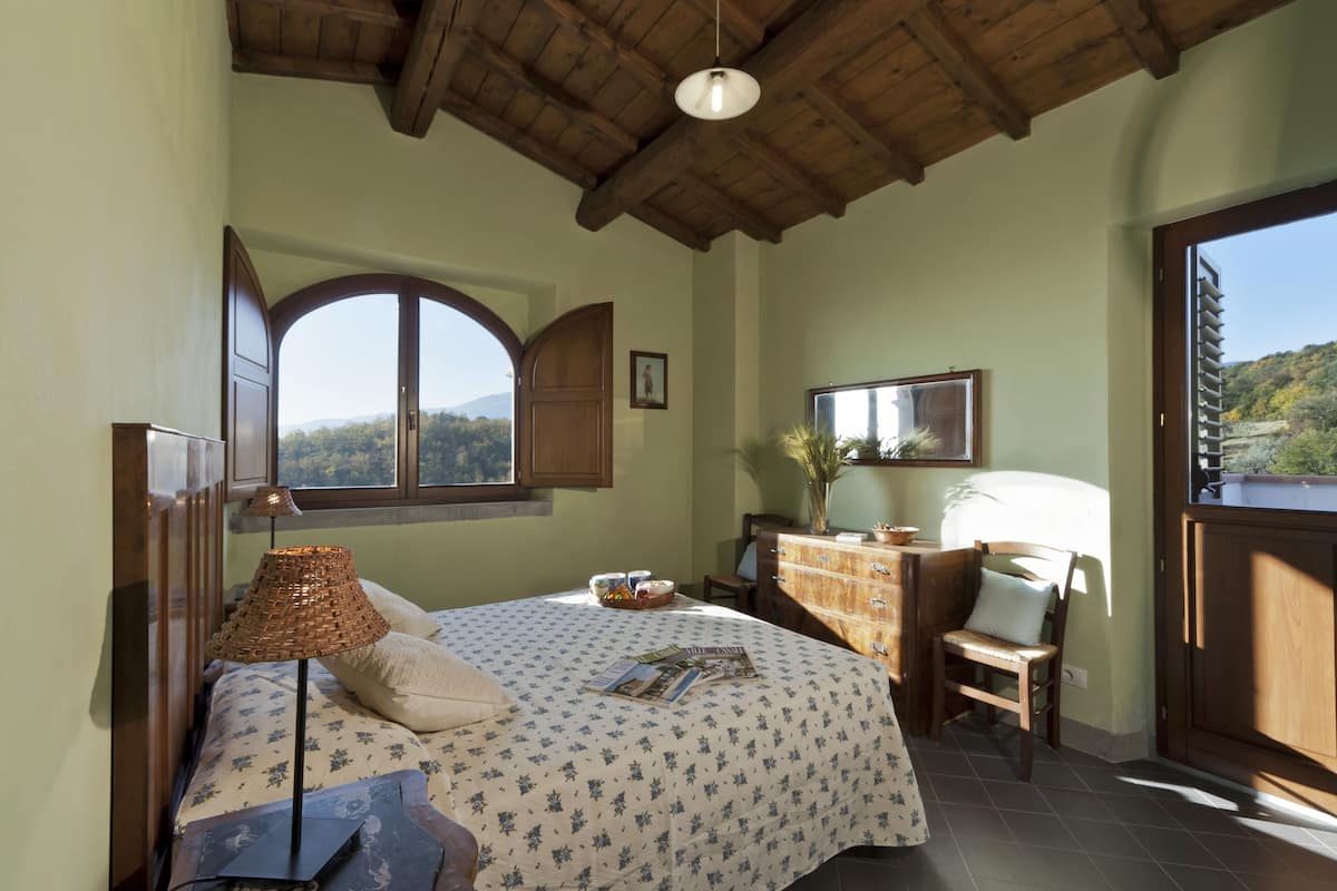 Ein Schlafzimmer mit Bett, Schreibtisch, Stuhl, Lampe, Fenster und Blick ins Freie.