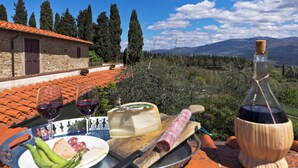 A table with a cheese platter, wine glasses, and a bottle of wine, set against a scenic mountain backdrop. - Castello di Pratelli (Figline e Incisa Valdarno)