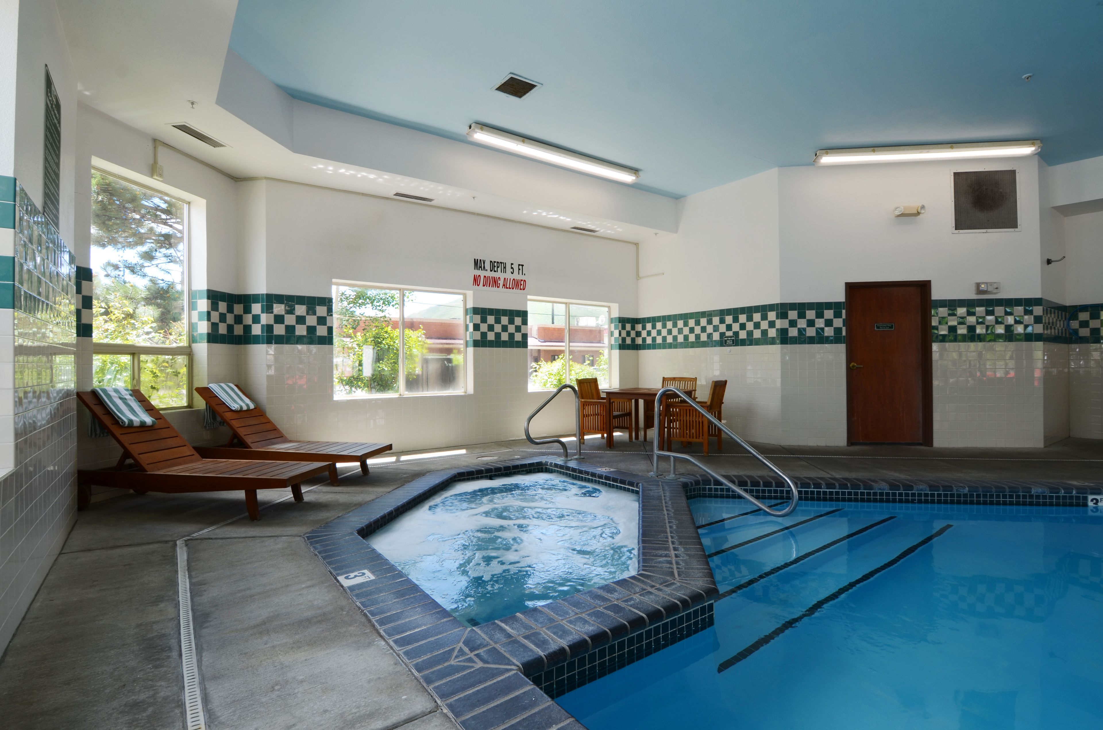 Zona de piscina con sillones de descanso, una bañera de hidromasaje y un borde de azulejos a cuadros.