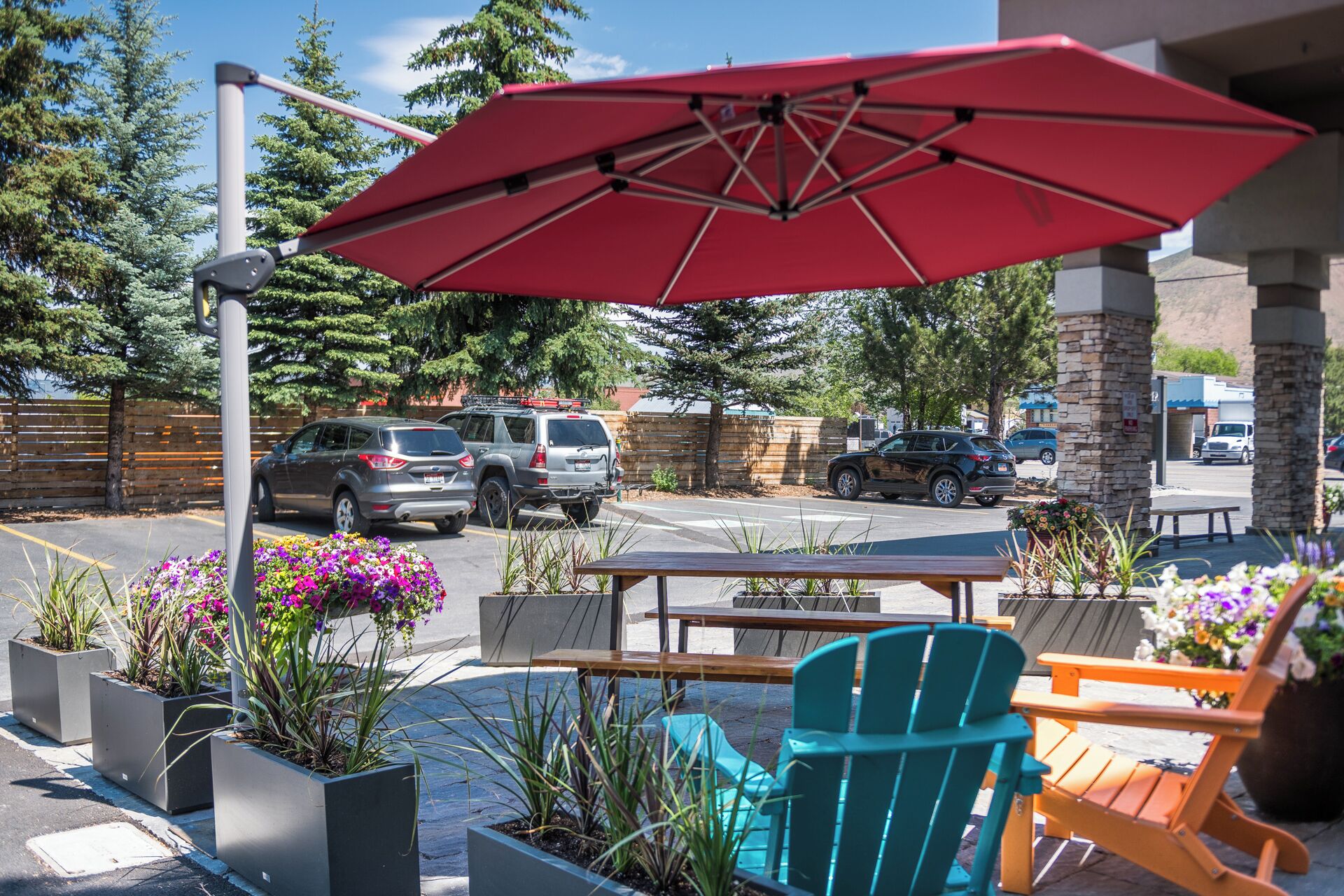 An outdoor seating area with a red umbrella, outdoor chairs, and planters with flowers.