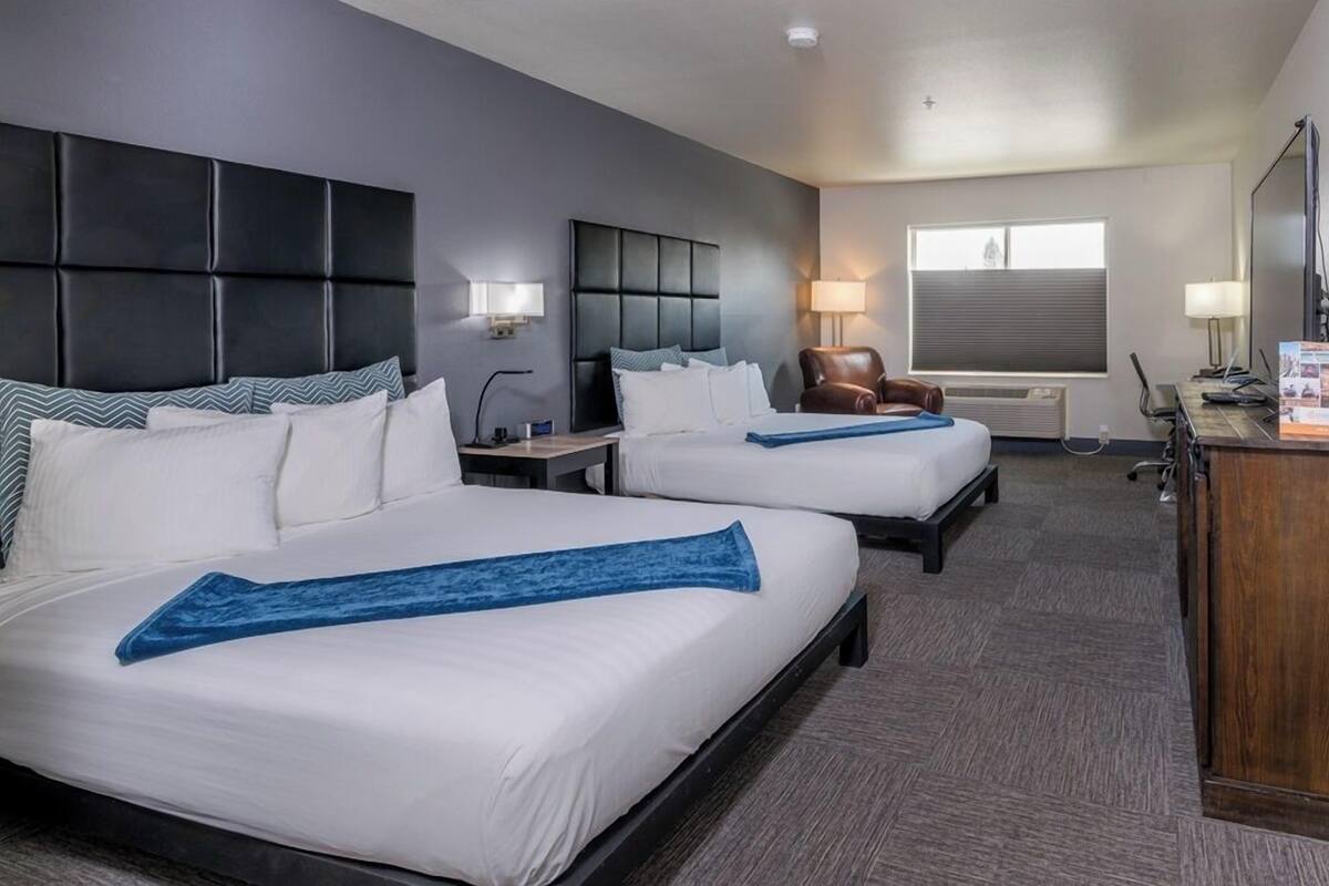 A hotel room with two beds, a desk, a chair, a lamp, and a window.