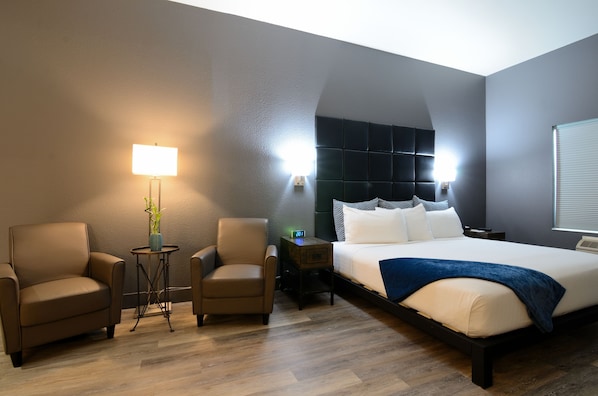 Une chambre d’hôtel comprenant un lit, deux fauteuils, une petite table avec une lampe et un luminaire fixé au mur.