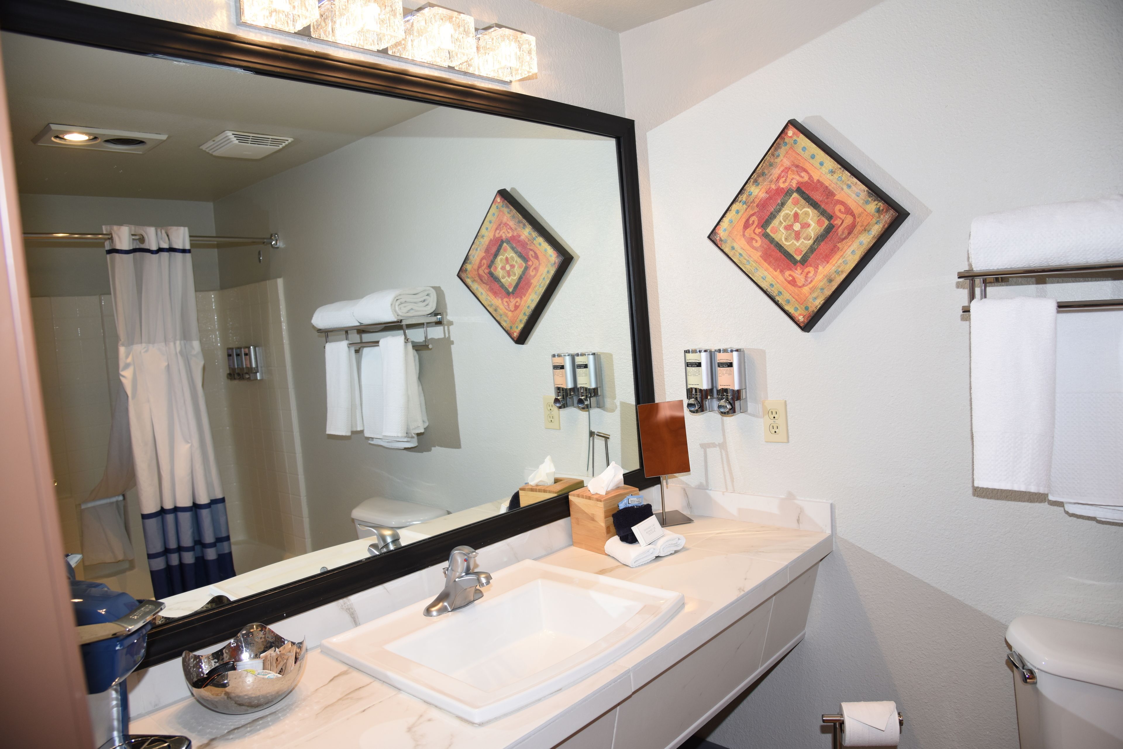 A bathroom with a large mirror, a sink, a shower, and two decorative wall pieces.