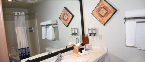 A bathroom with a large mirror, a sink, a shower, and two decorative wall pieces.