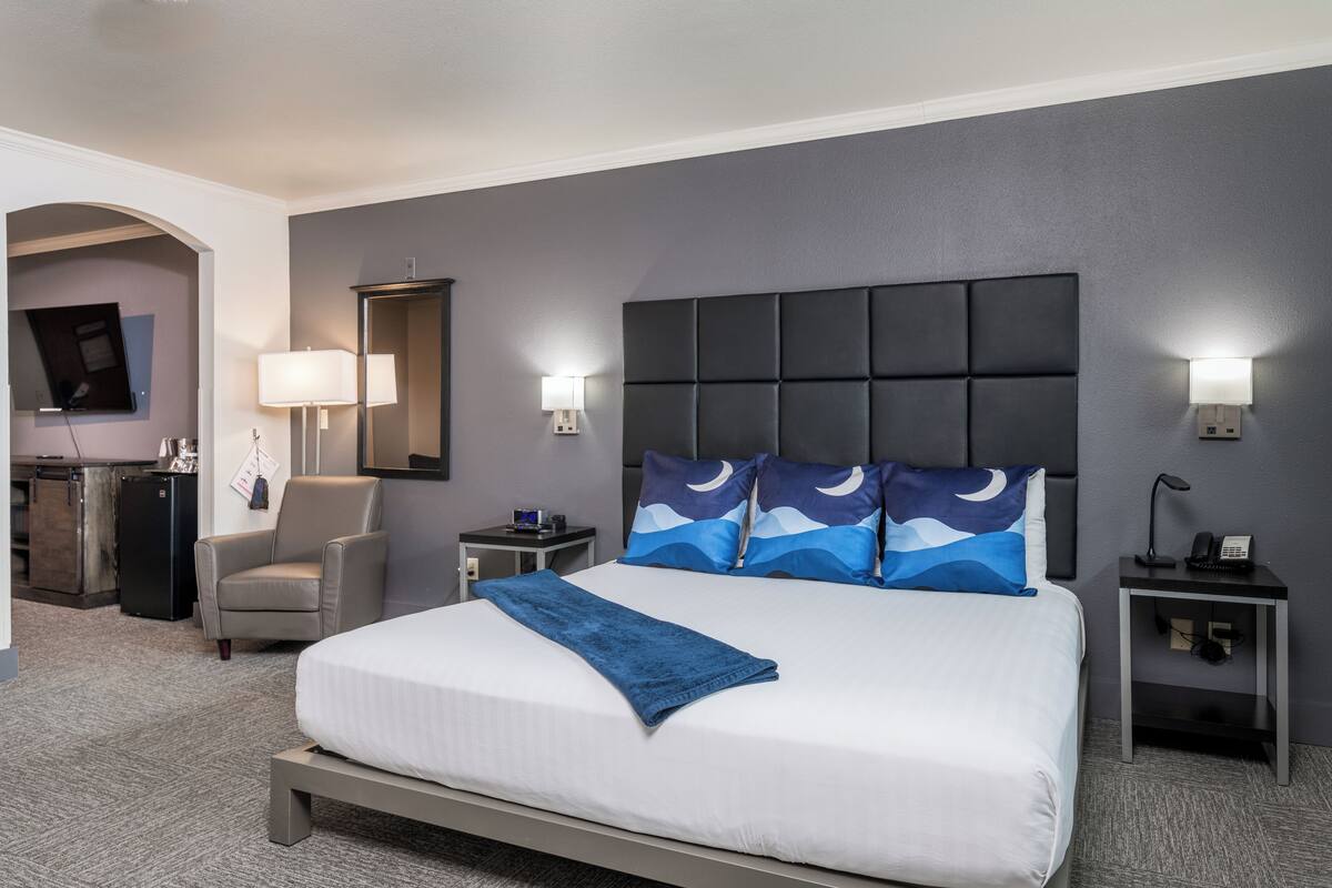 A modern hotel room with a large bed, a desk, a chair, and a TV mounted on the wall.
