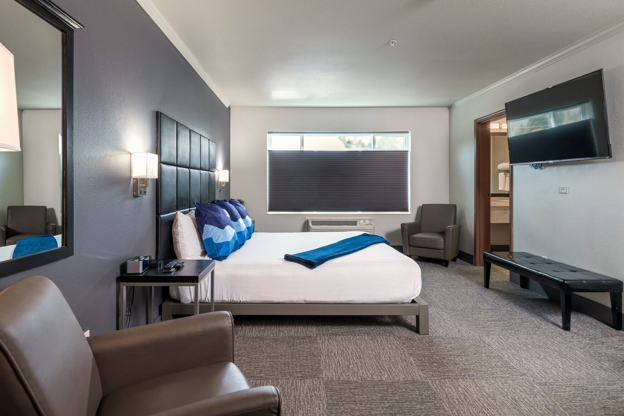 Habitación de hotel con una cama grande, un escritorio, una silla, un televisor y una ventana con persianas.