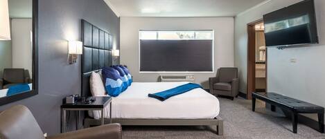 Habitación de hotel con una cama grande, un escritorio, una silla, un televisor y una ventana con persianas.