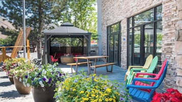 Un espace extérieur aménagé avec un belvédère, des tables en bois, des fauteuils Adirondack aux couleurs vives et des plantes en pot.
