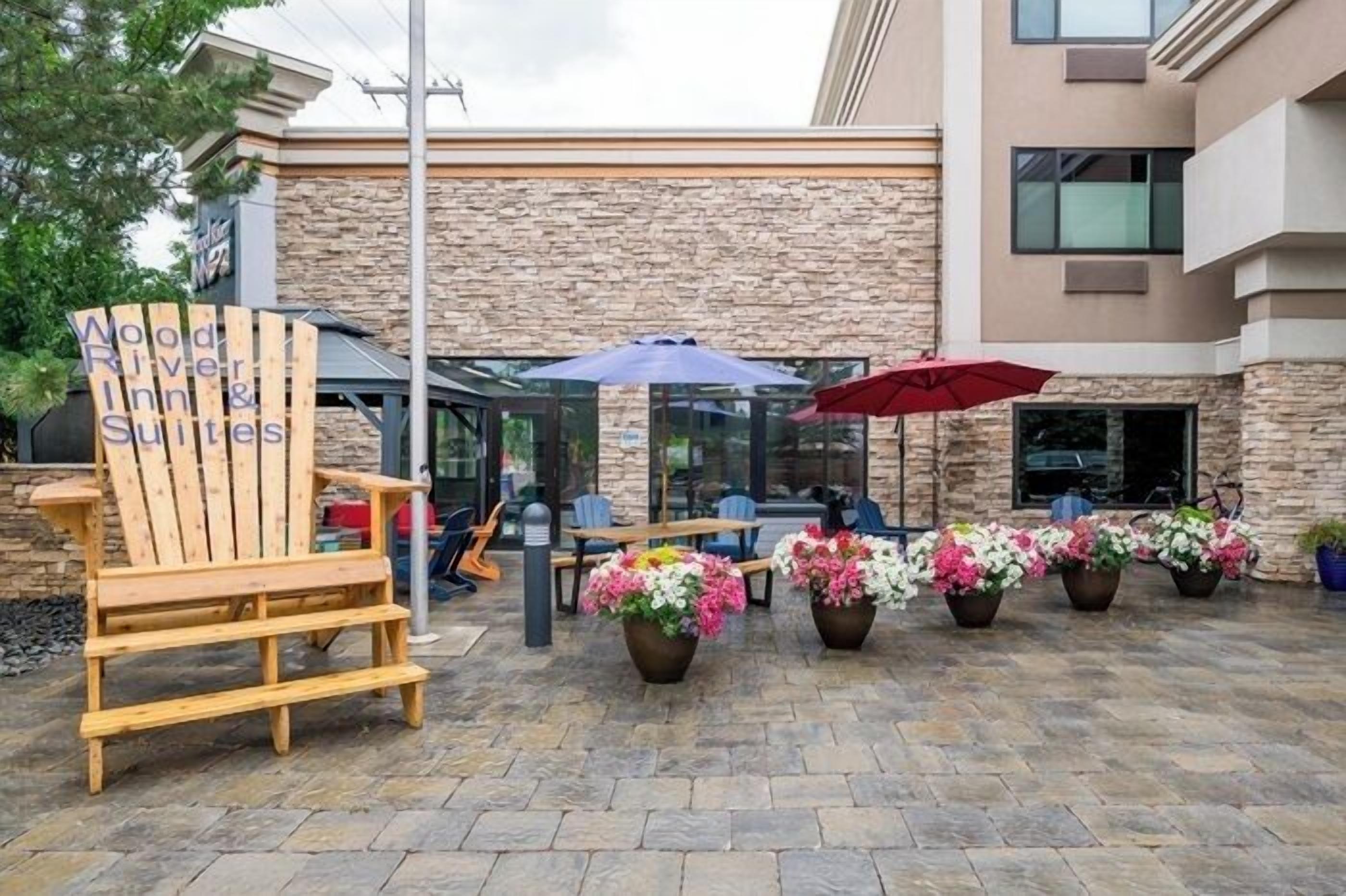 An outdoor seating area with Adirondack chairs, potted plants, and umbrellas at Wood River Inn & Suites.