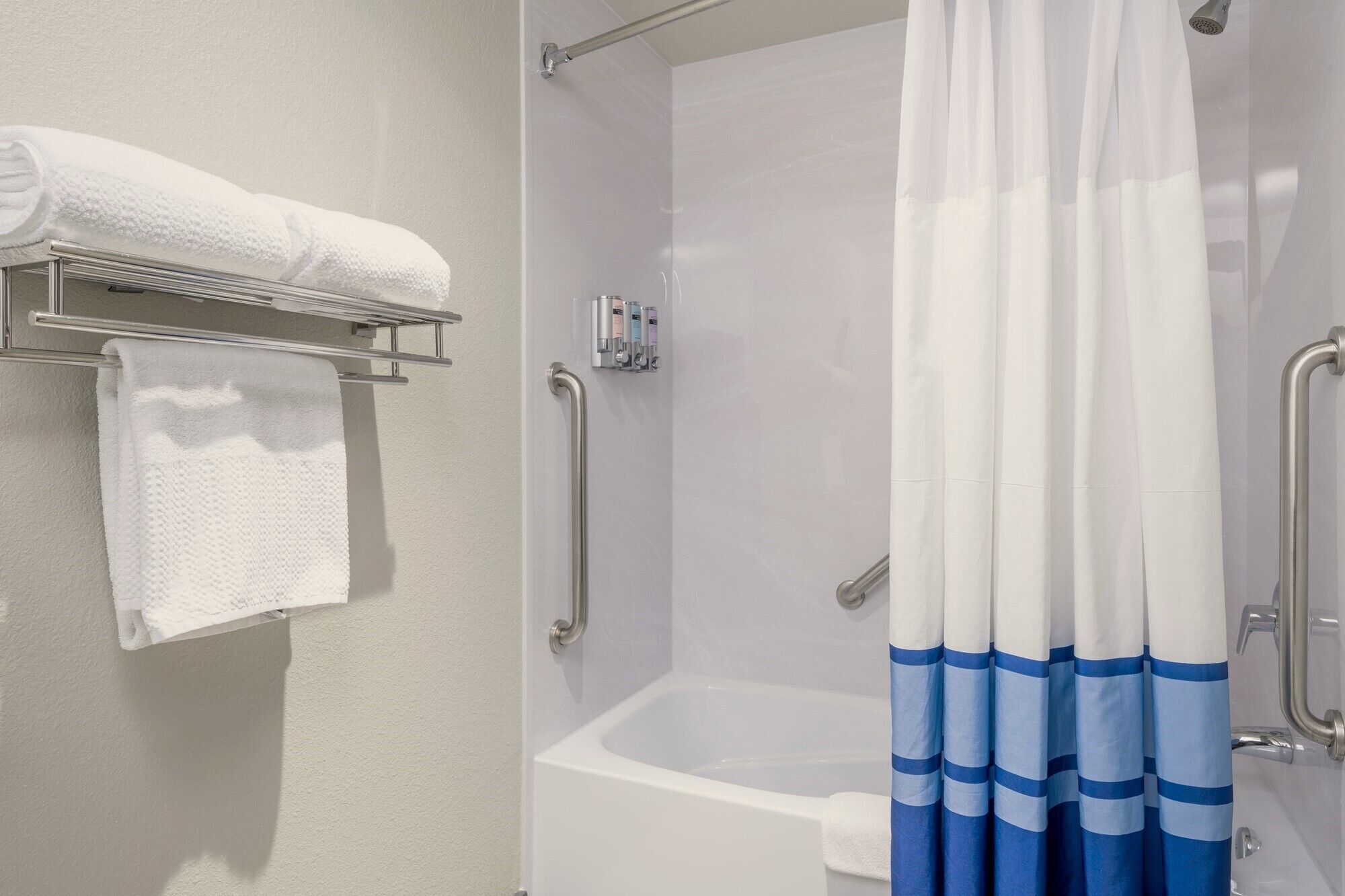 Een badkamer met een wit bad, een douche met een witte gordijn en een handdoekrek met een opgevouwen handdoek.