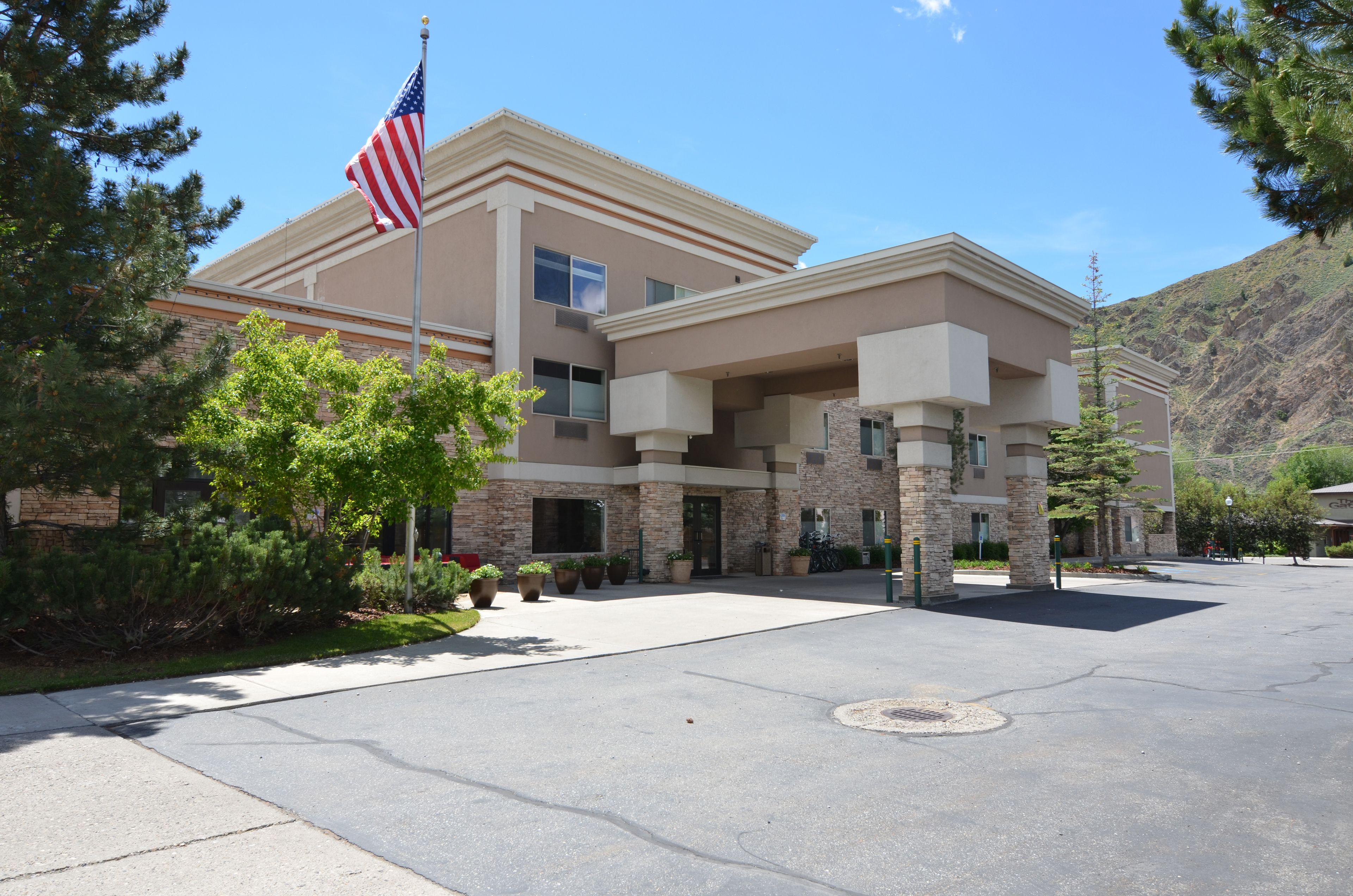 A two-story building with a flagpole, a paved driveway, and a mountain backdrop.