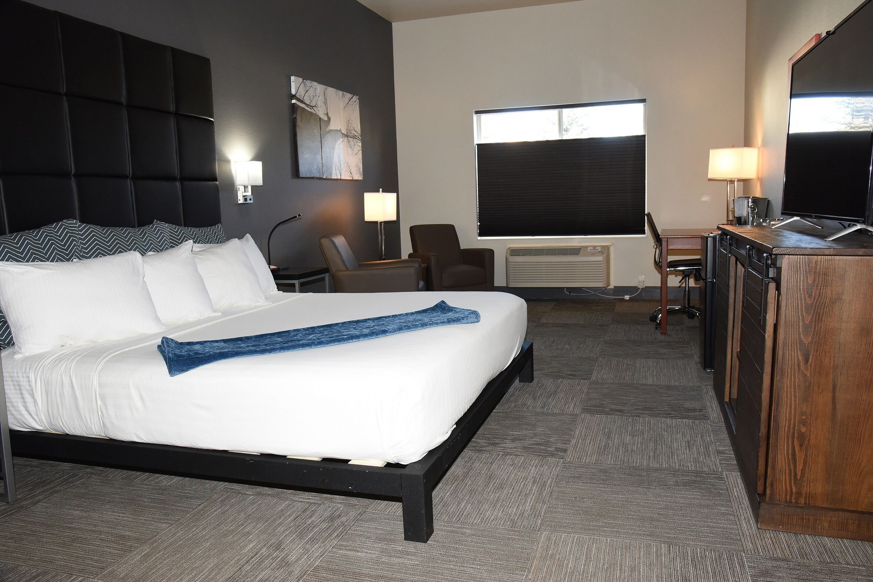 Quarto de hotel com uma cama grande, uma escrivaninha, uma cadeira e uma televisão.