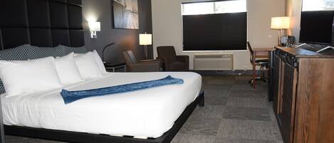 Quarto de hotel com uma cama grande, uma escrivaninha, uma cadeira e uma televisão.