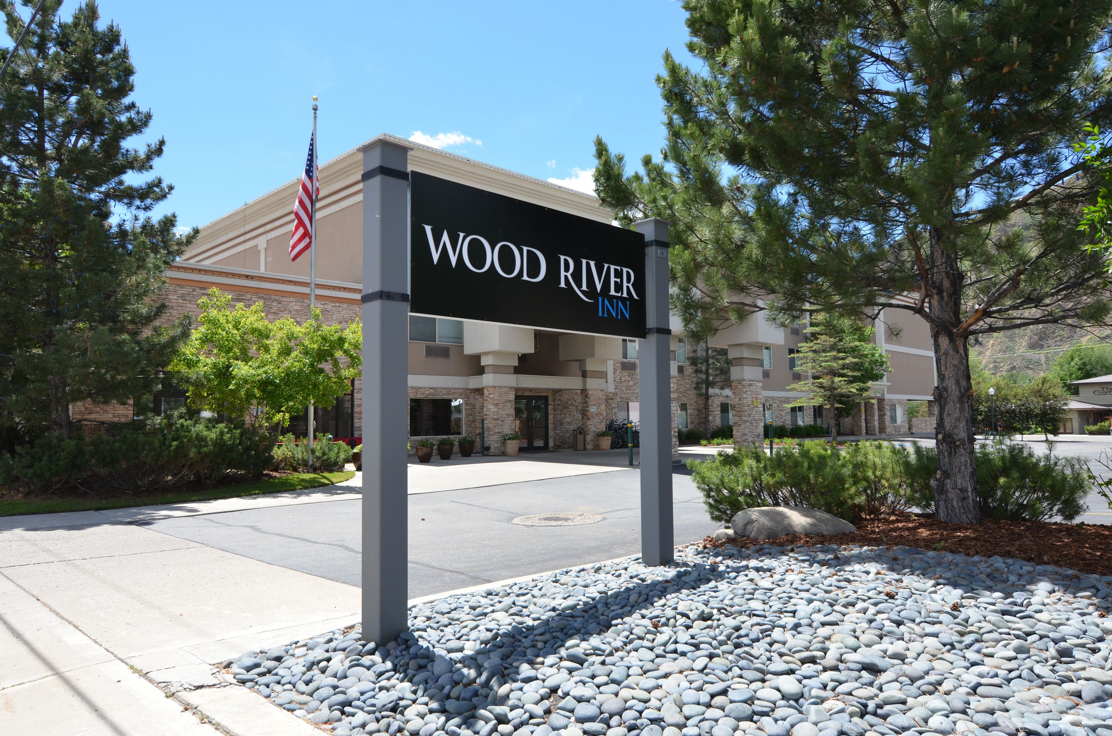 Cartel de Wood River Inn, con un edificio de piedra, una bandera y un área ajardinada.
