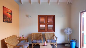 A room with a wooden ceiling, a table with chairs, a fan, and a blue trash bin. - West Hill Bungalows (Sabana Westpunt)