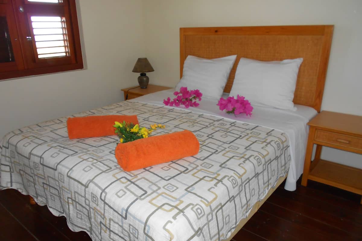 A neatly made bed with a patterned bedspread, two pillows, and decorative orange towels.