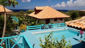 A pool area with a clear view of the ocean, a covered seating area, and a staircase leading to a higher level. - West Hill Bungalows (Sabana Westpunt)