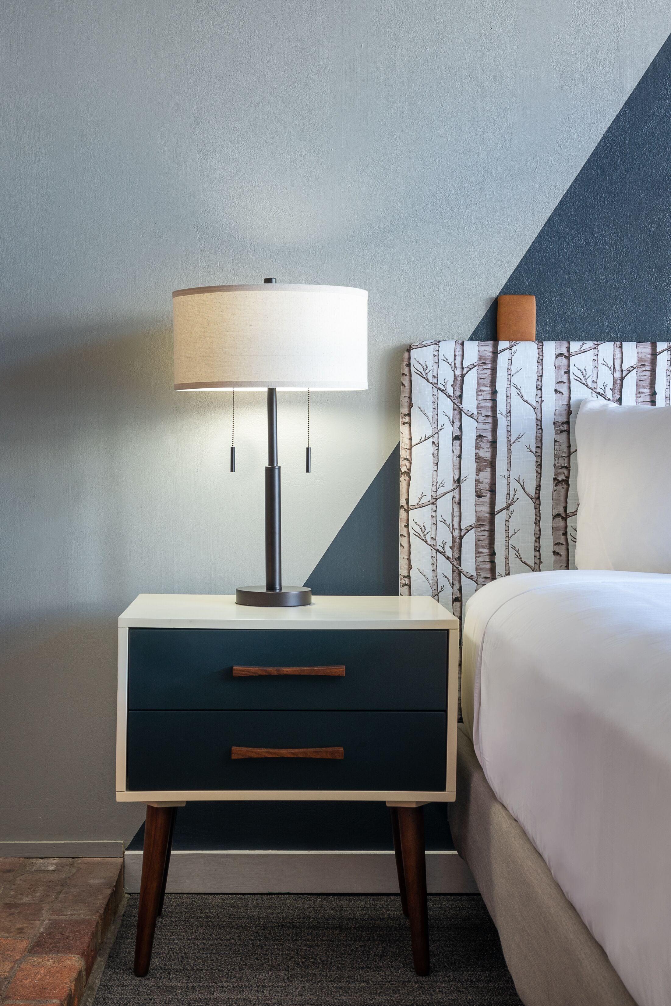 Cama bem arrumada com edredom branco e cabeceira estampada com padrão de árvore.