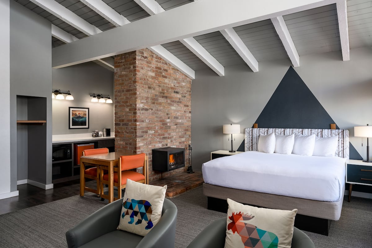 A modern hotel room with a large bed, a fireplace, a dining area, and a cozy seating space.