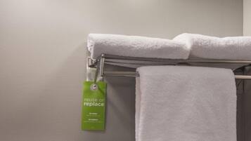 A bathroom with three wall-mounted lights, a towel rack with two white towels, and a green reusable or replaceable tag.